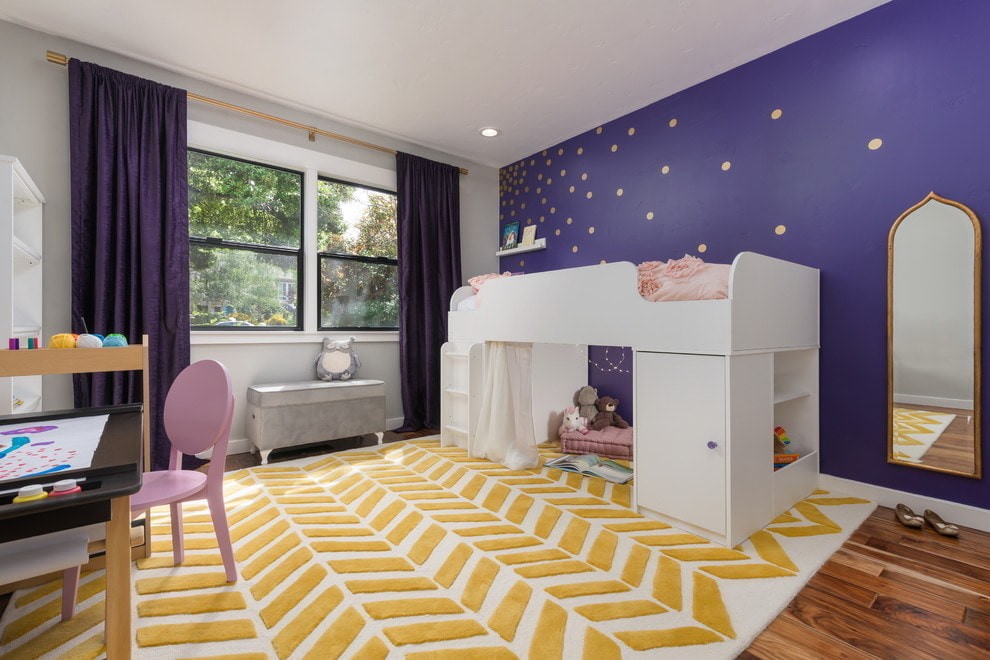 Высокая детская кровать на фоне стены фиолетового цвета