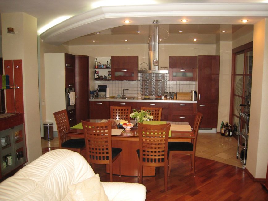 Зонирование пространства кухни-гостиной при помощи стола, потолка и напольного покрытия